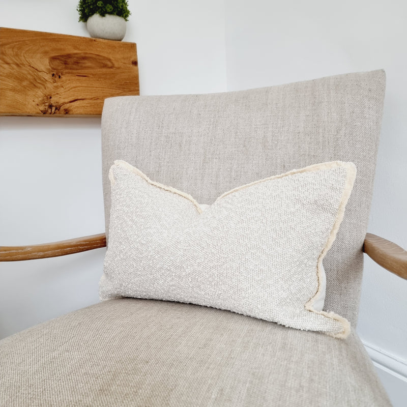 A cream rectangle boucle cushion, sat on a cream armchair