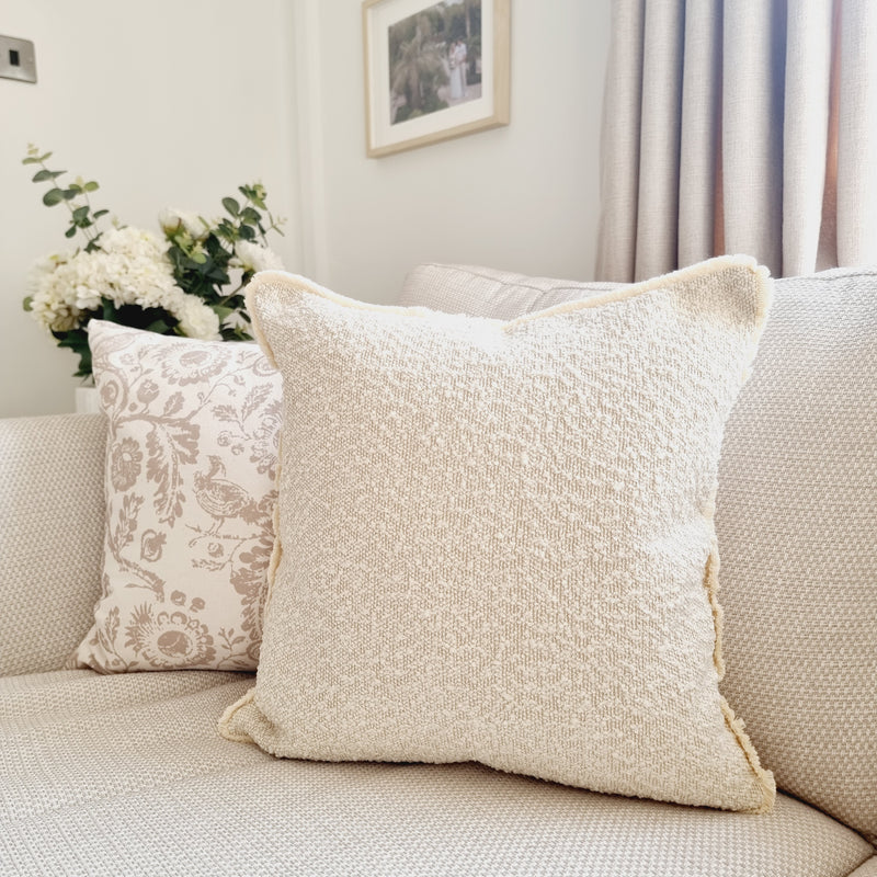 square cream boucle cushion with a frayed edge. Sat on a cream sofa