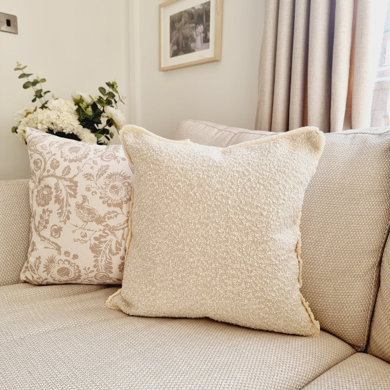 square cream boucle cushion with a frayed edge. Sat on a cream sofa