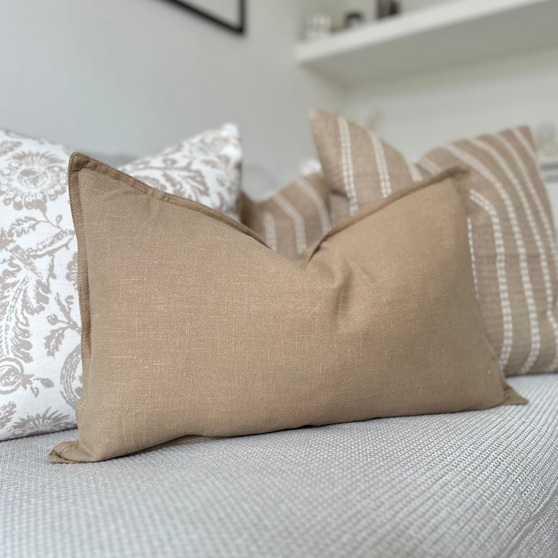 Beige Rectangle Linen Cushion sat in front of similar coloured cushions on a cream sofa