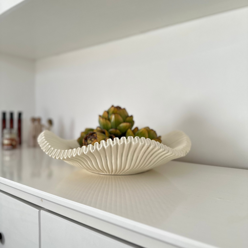 White scalloped edge decorative large bowl, with decorative green artichokes inside. Sat in the centre of a white sideboard