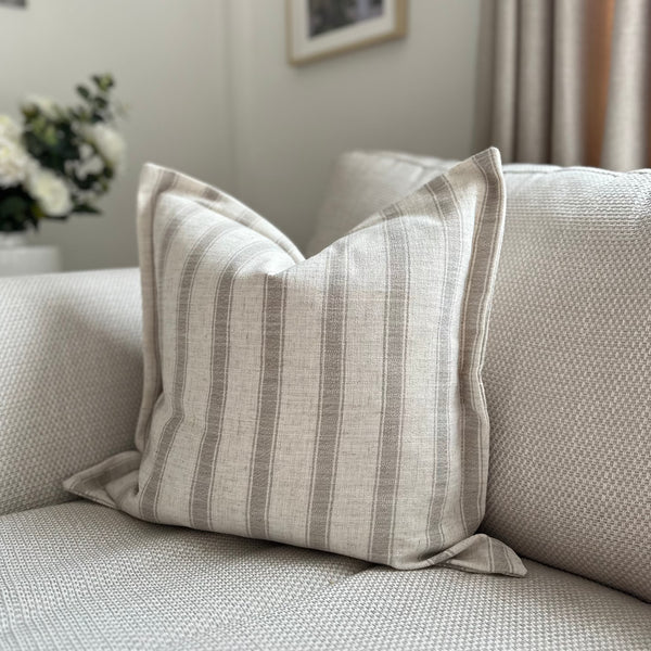 Cream Square cushion with a soft taupe thick vertical stripe. Flanged edge. Sat on a cream sofa