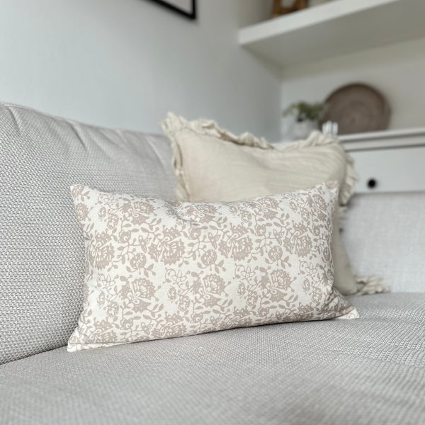 rectangle cream cushion with delicate beige floral details all over. Cushion sat on a cream sofa