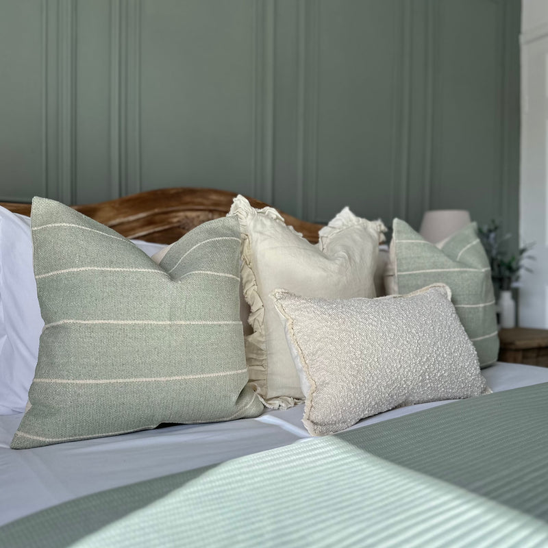 set of 4 cushions. 3 square cushions lined up on a bed 2 duck egg blue with cream stripes with a cream cushion with ruffled edges in the middle of both. One rectangle cream boucle cushion sat in front.