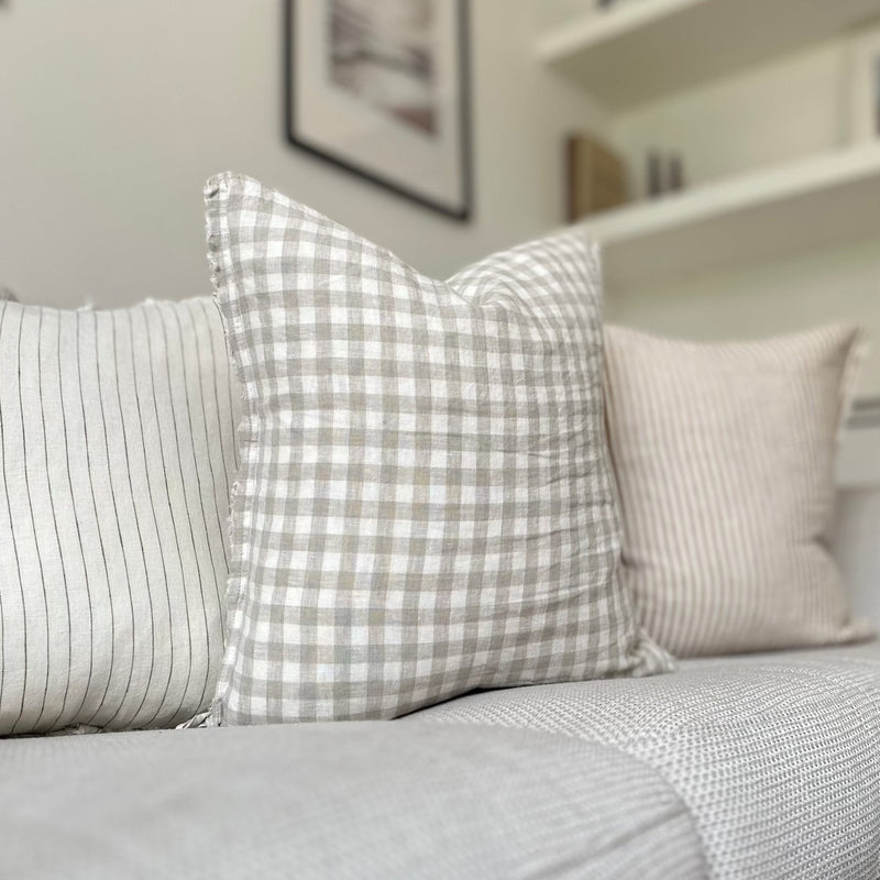 Square cream cushion with a beige gingham print, sat on a cream sofa.