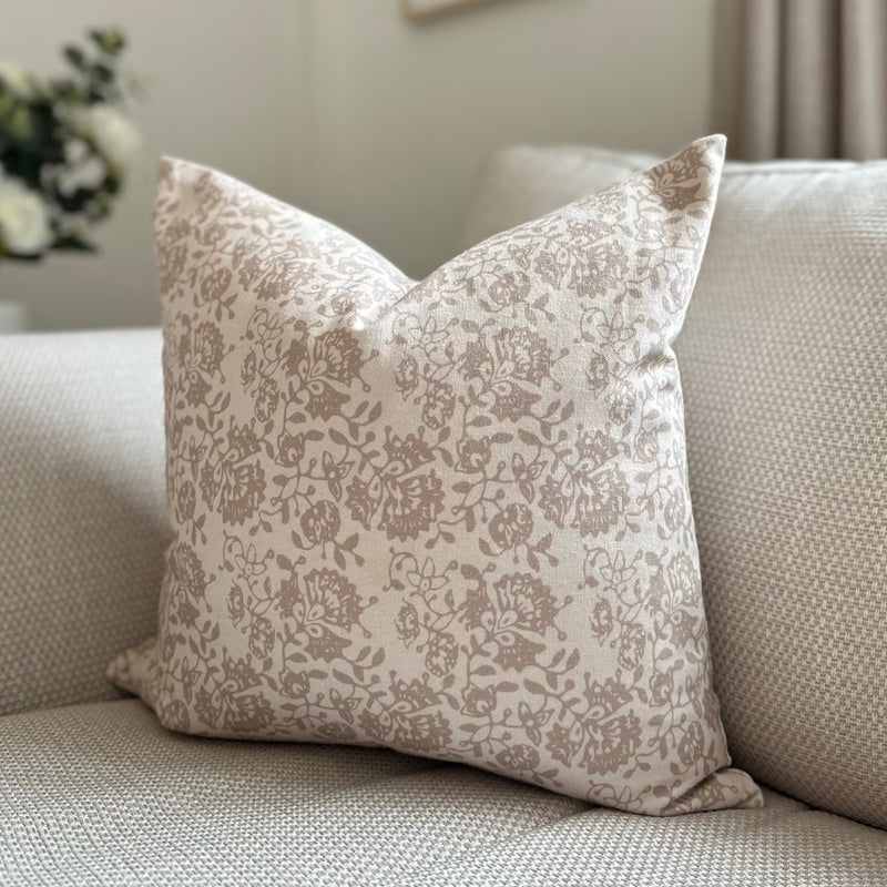 square cream cushion with a delicate taupe/beige floral pattern motif all over front and back. Sat on a cream sofa