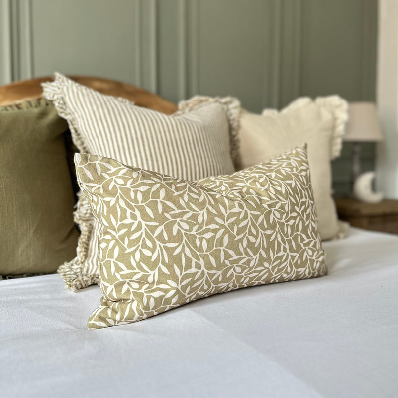 olive rectangle cushion with cream olive leaves print. Sat on white bedding . With green tones around the room.
