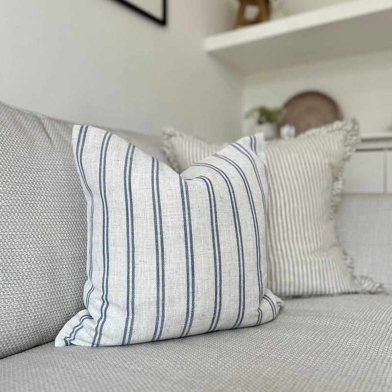 Light cream cushion with navy blue vertical double stripe motif all the way around the cushion. sat on a light cream sofa