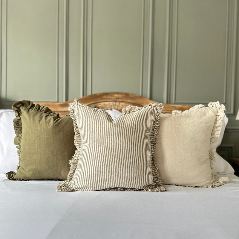 cream cushion with a ruffled edge and with a thick chunky repetitive vertical stripe. Sat on a bed with a green wall background.