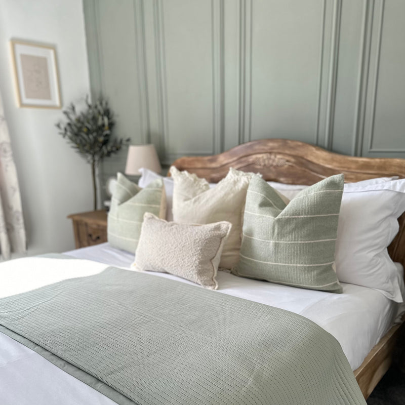 set of 4 cushions. 3 square cushions lined up on a bed 2 duck egg blue with cream stripes with a cream cushion with ruffled edges in the middle of both. One rectangle cream boucle cushion sat in front.