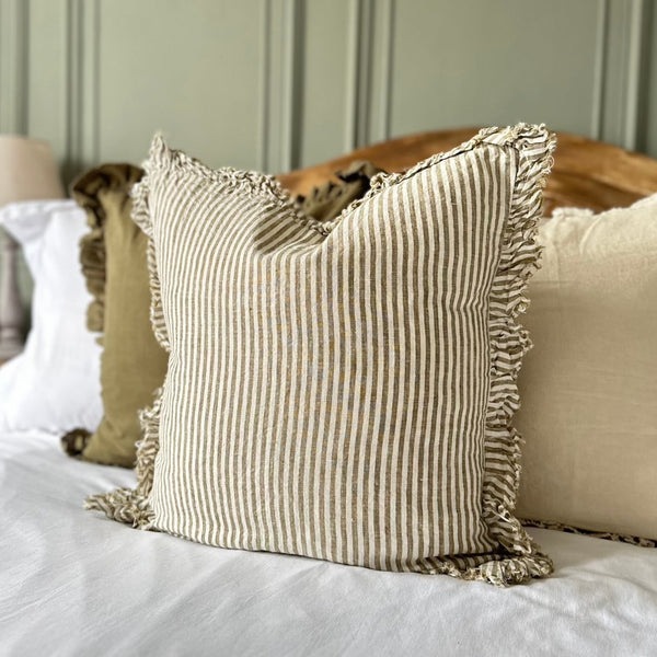cream cushion with a ruffled edge and with a thick chunky repetitive vertical stripe. Sat on a bed with a green wall background.