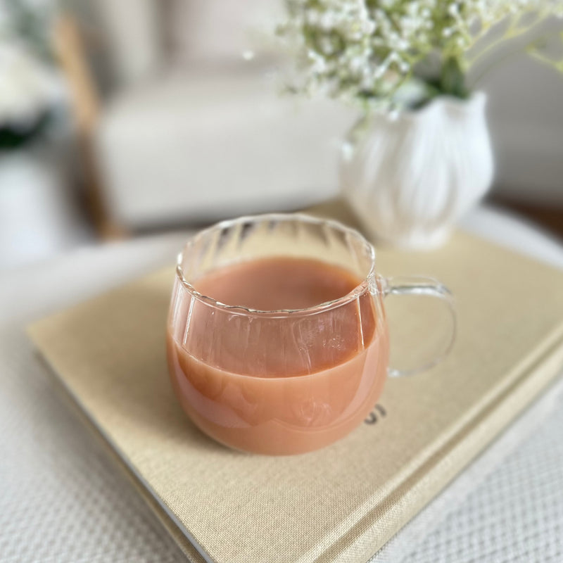 clear glass ribbed mug with a handle. Filled with tea sat on a stack of books.