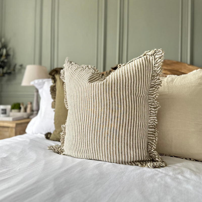 Close up of cream cushion with a ruffled edge and with a thick chunky repetitive vertical stripe. Sat on a bed with a green wall background.