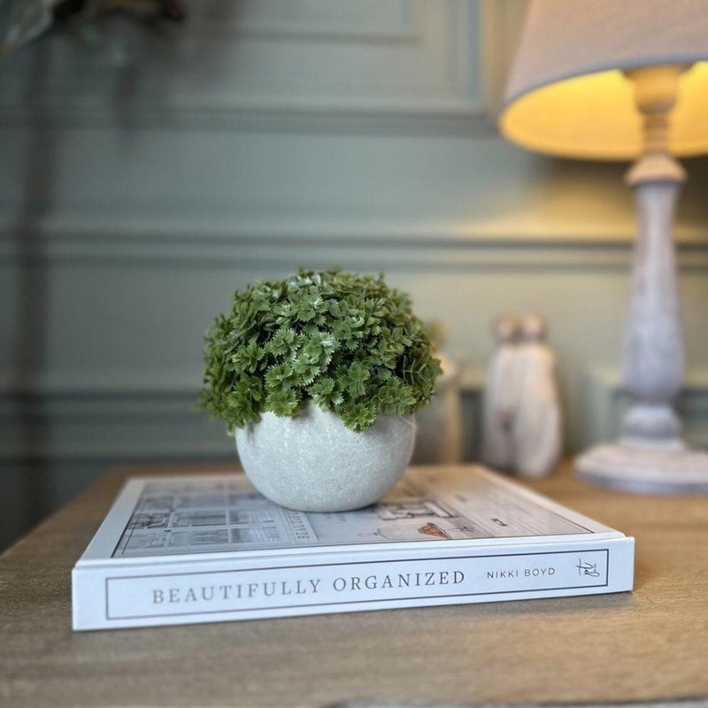 FAUX MINI HEBE BUSH IN GREY STONE POT, SAT ON A WHITE BOOK ON A WOODEN BEDSIDE TABLE