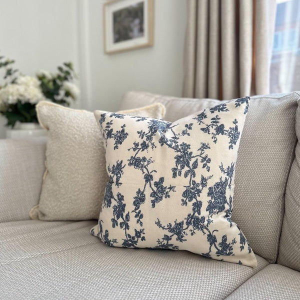square cream cushion with a large navy blue floral print. Sat on a cream sofa.