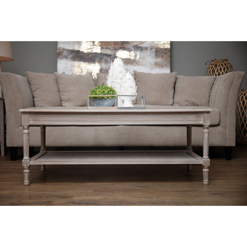 Wooden whitewash rattan coffee table with a rattan bottom shelf for storing books, magazines and more. Sat in a living room in front of a cream sofa.