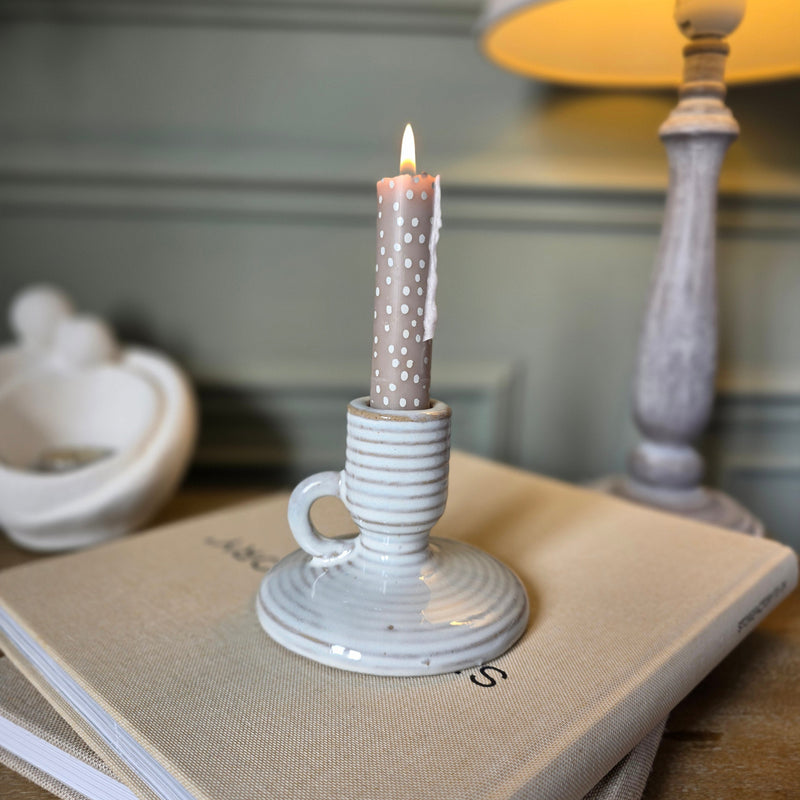 Neutral Ceramic candle holder with handle sat on a bedside table holding a tall candle stick