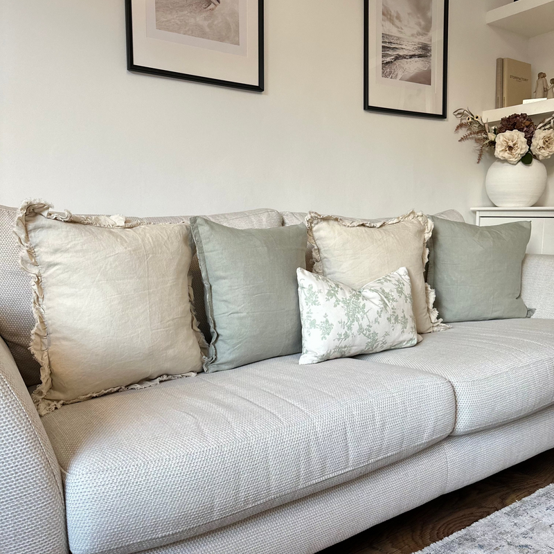 set of 5 sage green or cream cushions . With a mixture of square plain cream, square plain green and 1 rectangle cream with sage green floral prints sat on a  cream sofa