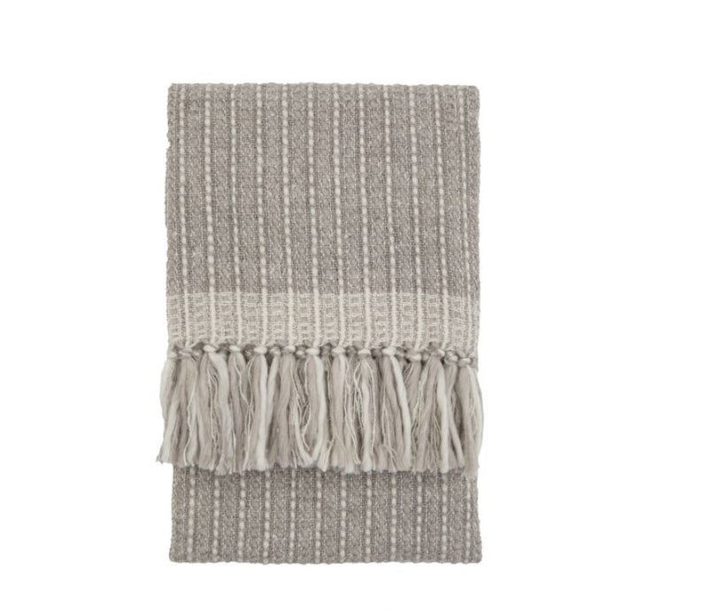 A soft grey throw with a subtle cream stich throughout with chunky tassels along the bottom