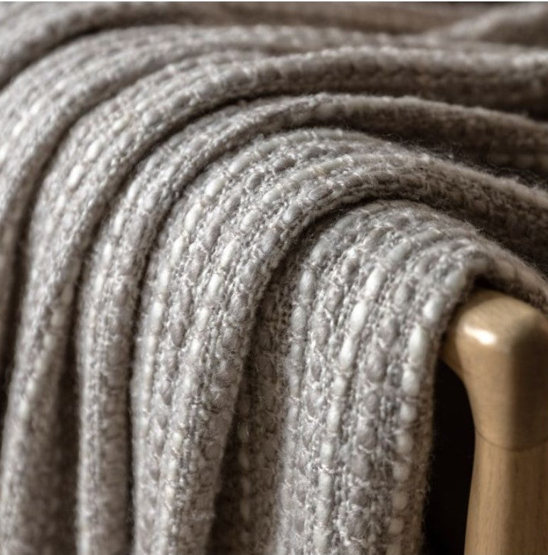 A close up of Kath and Kin's soft grey throw with a subtle cream stich throughout with chunky tassels along the bottom