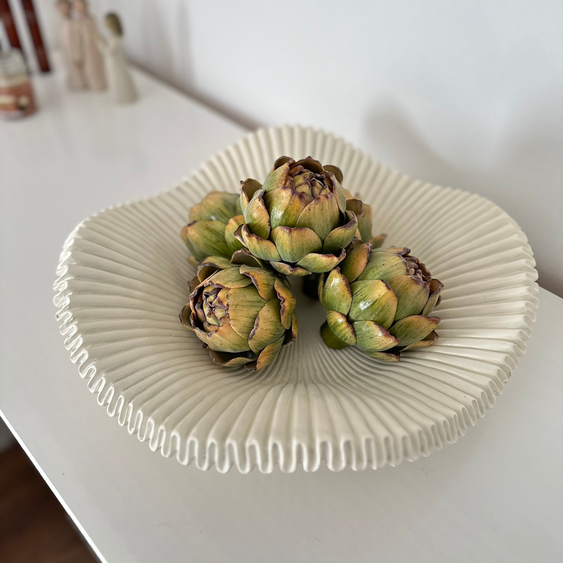 Birds eye view of white scalloped edge decorative large bowl, with decorative green artichokes inside. Sat in the centre of a white sideboard