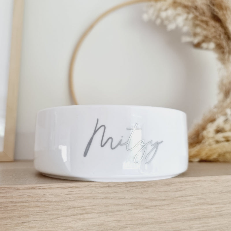 White ceramic pet bowls sat on pine shelf with "Mitzy" written in script font on front of bowl in silver