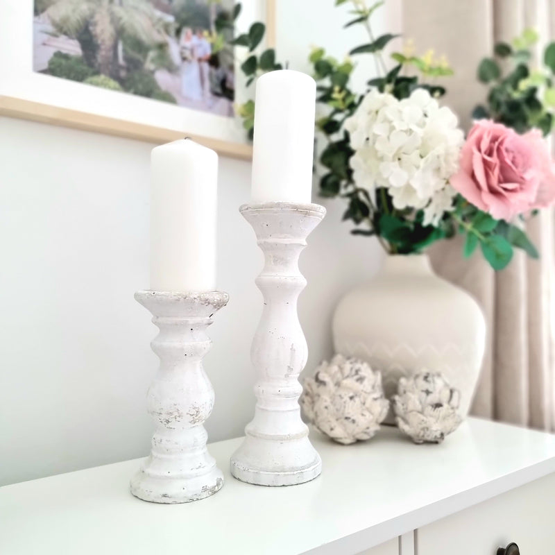 small and large white stone pillar candle holder side by side, holding large white candles. Romantic style