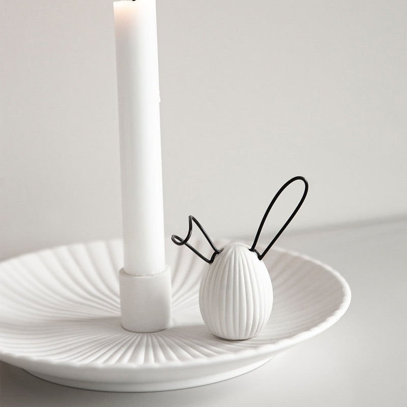 A decorative white egg with a ribbed design and black wire ears, adding a playful touch to any space. The unique design and color scheme make it a versatile addition to any decor style, perfect for Easter or springtime. Ideal for display on shelves, mantels, or desks, and makes a great gift for friends, family, or co-workers.