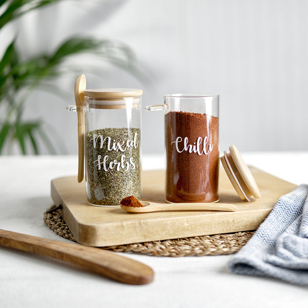 Two glass spice jars with an eco friendly bamboo lid and serving spoon, with custom personalised wording for Mixed Herbs and Chilli