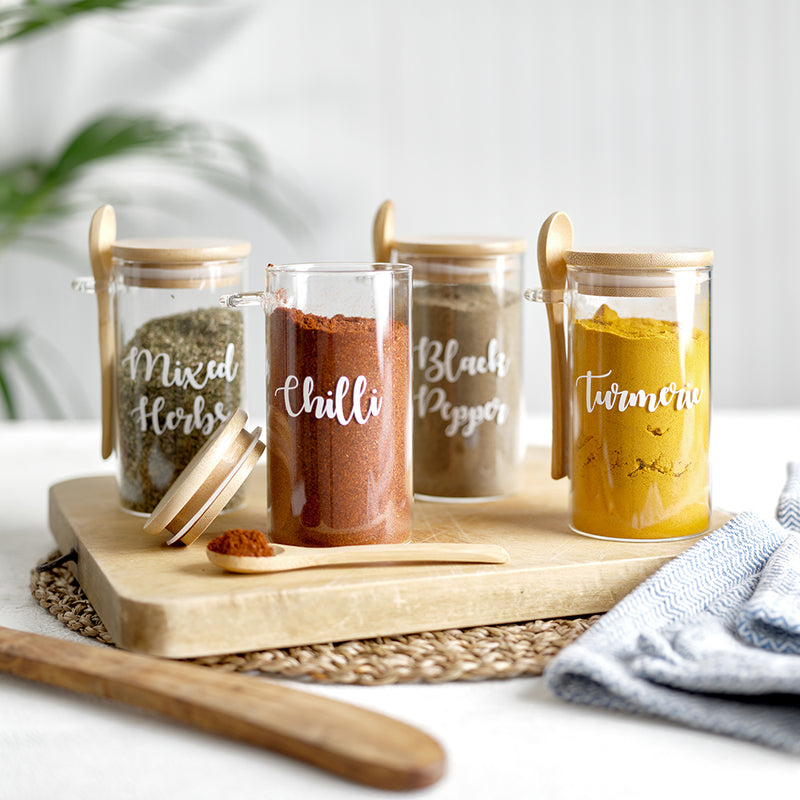 Four glass spice jars with an eco friendly bamboo lid and serving spoon, with custom personalised wording for Mixed Herbs, Chilli, Black Pepper and more